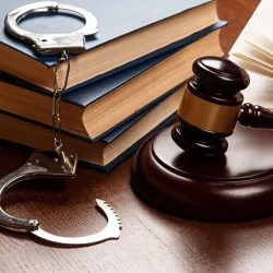 A pair of handcuffs laying on a table next to some law books and a gavel